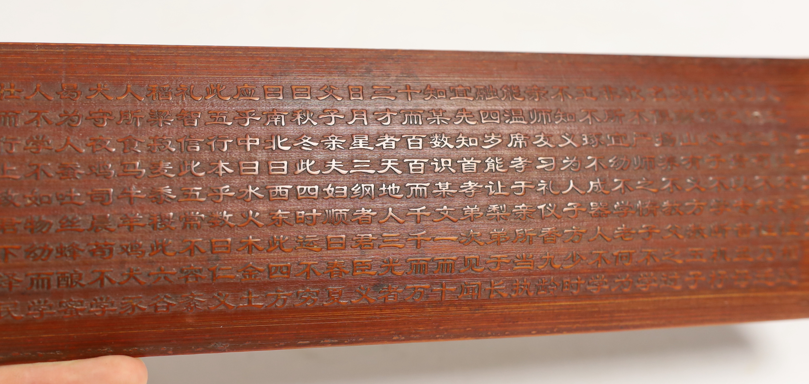 A Chinese bamboo inscribed wrist rest, carved in relief with columns of calligraphy, 30cm wide